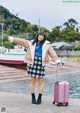 A woman standing next to a pink suitcase on a dock.