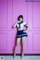 A woman in a sailor outfit posing in front of a pink wall.